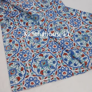 May include: White fabric with a blue and red floral pattern. The fabric has a repeating pattern of stylised flowers and leaves. The fabric is folded in half and the edges are visible.