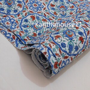 May include: A white fabric with a blue and red floral pattern. The fabric is folded and has a textured surface.