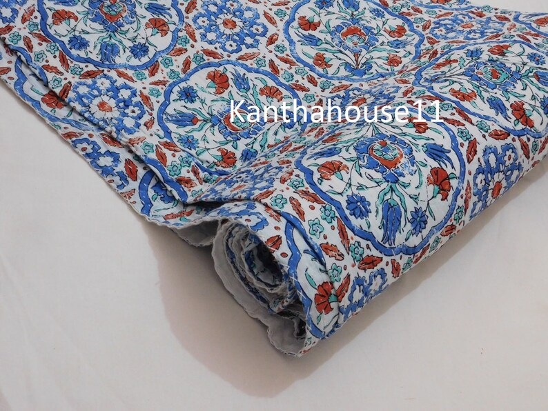 May include: A white fabric with a blue and red floral pattern. The fabric is folded and has a textured surface.