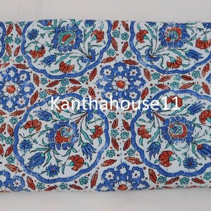 May include: White cotton fabric with a blue and red floral pattern. The fabric has a distressed look and features a repeating pattern of stylised flowers and leaves. The text "Kantha house 11" is visible in the centre of the fabric.