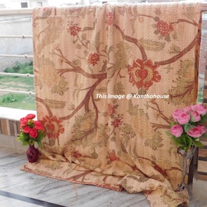 Puede incluir: Una colcha kantha beige con un patr&oacute;n floral en tonos rojos, verdes y marrones. La colcha est&aacute; doblada y se muestra en un balc&oacute;n.