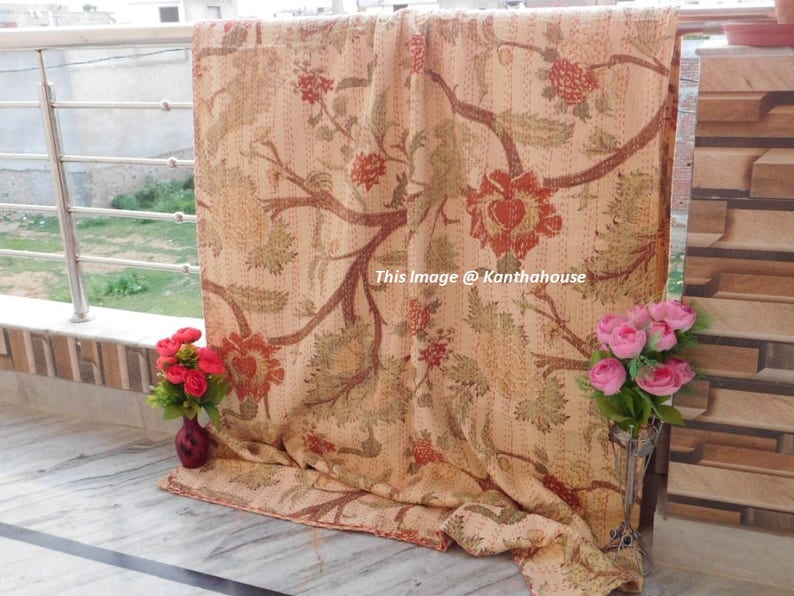 Puede incluir: Una colcha kantha beige con un patr&oacute;n floral en tonos rojos, verdes y marrones. La colcha est&aacute; doblada y se muestra en un balc&oacute;n.