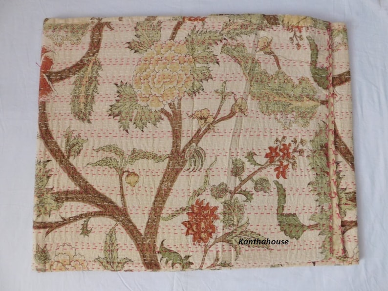 Puede incluir: Una colcha kantha de color crema con un patr&oacute;n floral en tonos verdes, marrones y naranjas. La colcha est&aacute; cosida a mano y tiene un borde deshilachado. El texto "Kantha House" es visible en la esquina inferior derecha.