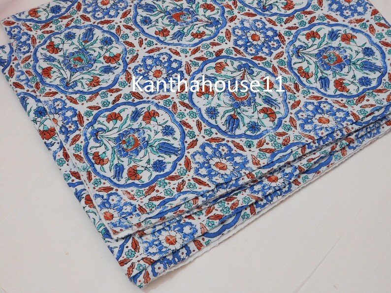 May include: A stack of white fabric napkins with a blue and red floral pattern. The pattern features stylised flowers and leaves in a repeating design.