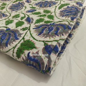 May include: White cotton fabric with a blue and green floral print. The fabric is folded and has a stitched edge. The text "Kantha house" is visible on the fabric.