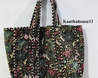 Op de afbeelding: Een zwarte tote bag met een bloemenpatroon in roze, groene en witte tinten. De tas heeft twee lange hengsels en is gemaakt van gestikt materiaal.