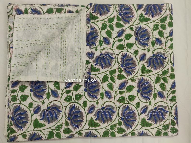 May include: A white cotton kantha quilt with a floral pattern in shades of blue, green, and gray. The quilt is hand-stitched and has a traditional Indian design. "Kantha House" is printed on the quilt.