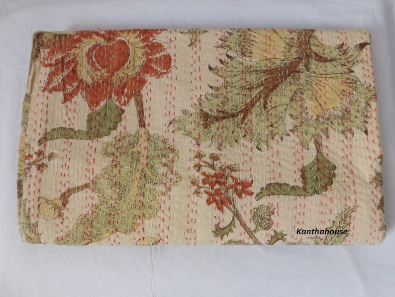 Puede incluir: Una colcha kantha beige con un patr&oacute;n floral en tonos de verde, marr&oacute;n y naranja. La colcha tiene un sutil patr&oacute;n de puntos rosas y el texto "Kantha House" es visible en la esquina inferior derecha.