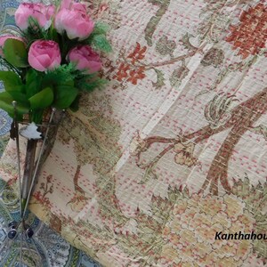 Puede incluir: Una colcha kantha blanca con un patr&oacute;n floral en tonos de rosa, verde y marr&oacute;n. La colcha est&aacute; cosida a mano y tiene una textura delicada. El texto "Kantha house" es visible en la esquina inferior derecha de la imagen.