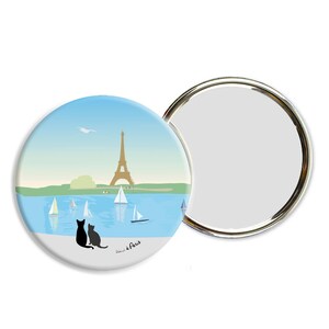 Peut inclure: Un miroir de poche rond. Le devant du miroir présente une illustration bleue et blanche de la tour Eiffel à Paris, en France. Deux chats noirs sont assis sur le rivage d'un lac avec des voiliers dans l'eau. Le texte "J'aime Paris" est imprimé au bas du miroir.