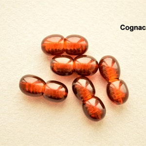 May include: Six brown glass beads with a ribbed texture. The beads are in the shape of two connected ovals. The beads are arranged in a cluster on a white surface. The word "Cognac" is written in black text above the beads.
