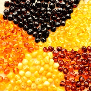 Peut inclure: Un ensemble de perles d'ambre de différentes couleurs, dont noir, orange, jaune et marron. Les perles sont disposées en cercle, mettant en valeur leurs diverses teintes et variations naturelles. Ces perles sont adaptées à la création de bijoux.