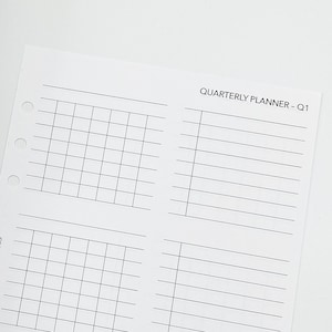 May include: A light beige leather planner with a snap closure next to a white paper with a quarterly planner grid and the text "QUARTERLY PLANNER - Q1". The paper has three-hole punches for binder use.