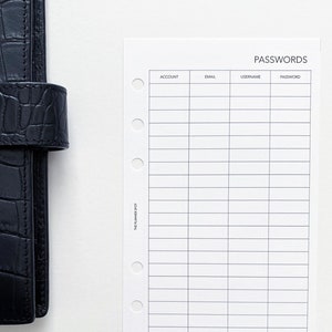 Puede incluir: Un planificador de cuero negro con un acabado texturizado se muestra junto a una hoja de registro de contraseñas blanca. La hoja de registro de contraseñas tiene columnas para cuenta, correo electrónico, nombre de usuario y contraseña. La palabra "PASSWORDS" está impresa en la parte superior de la hoja.
