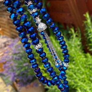 Op de afbeelding: Een blauwe gebedsketting met zilveren accenten. De kralen zijn gefacetteerd en hebben een metallic glans. De ketting is geregen aan een zilveren ketting en heeft een zilveren kwast.