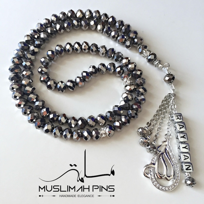 Op de afbeelding: Een zwarte kristallen gebedsketting mala met een zilveren bedel en een zilveren naamschild met de tekst "Rayyan".