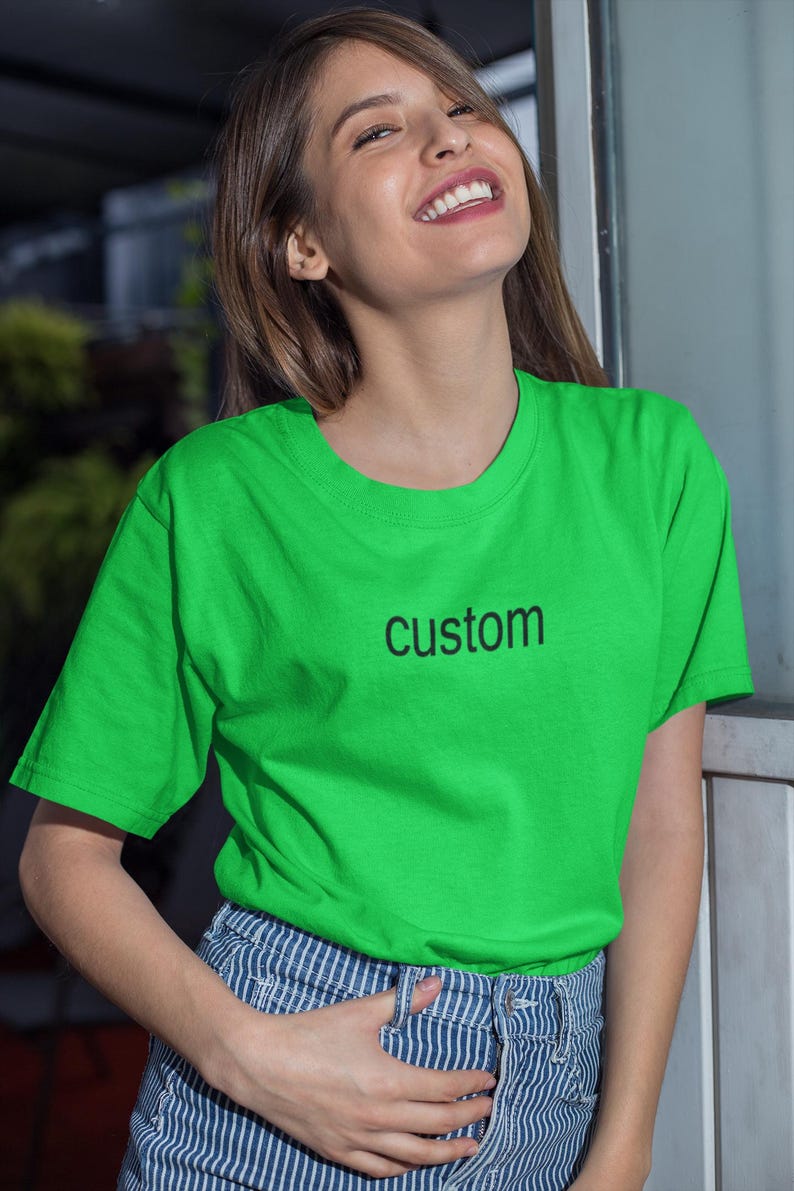 May include: A woman wearing a bright green t-shirt with the word "custom" printed on the front. She is smiling and has her hand in her pocket.
