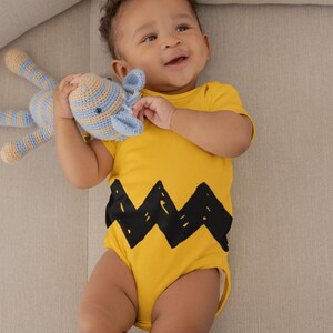 Peut inclure: Un b&eacute;b&eacute; portant un body jaune avec un motif en zigzag noir, tenant un jouet en crochet ray&eacute; bleu et beige.
