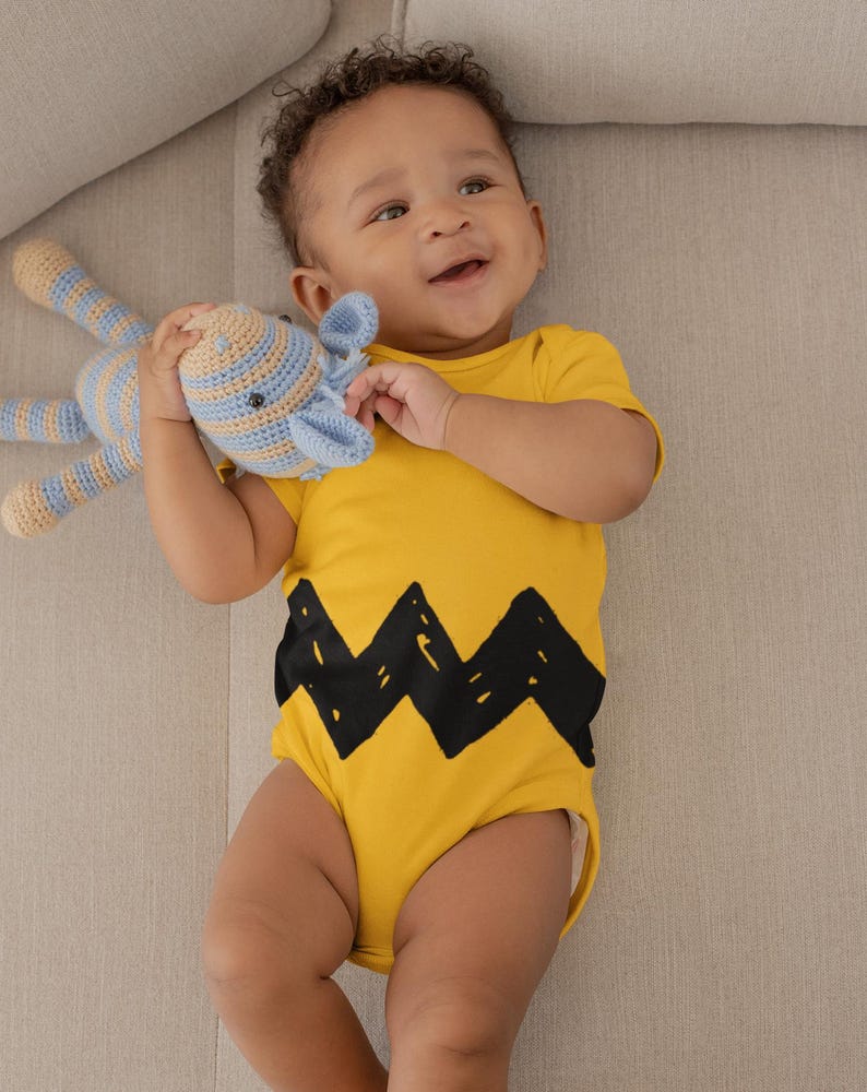 Peut inclure: Un b&eacute;b&eacute; portant un body jaune avec un motif en zigzag noir, tenant un jouet en crochet ray&eacute; bleu et beige.