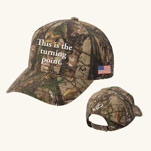 May include: Camouflage baseball cap with the text "This is the turning point." An American flag patch is on the side. The cap is designed with a curved brim and adjustable strap.