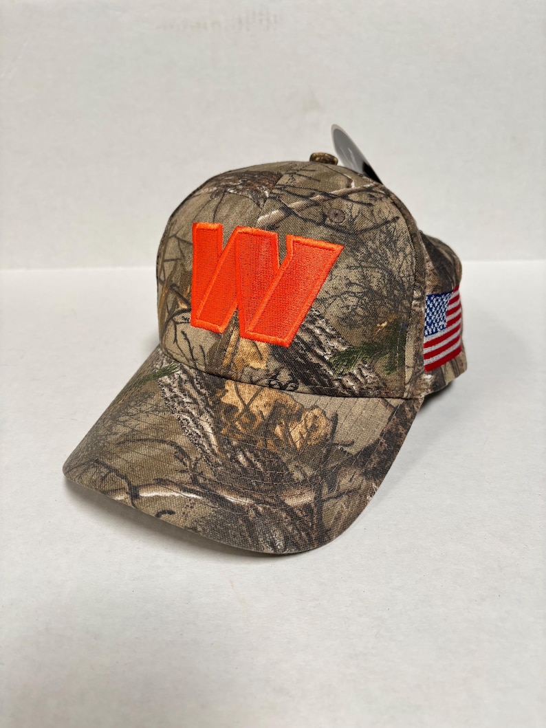 Pu&ograve; includere: Un cappellino da baseball mimetico con una "W" arancione ricamata sul davanti. Il cappellino ha una visiera curva e una toppa con la bandiera americana sul lato. Progettato per attivit&agrave; all'aperto.