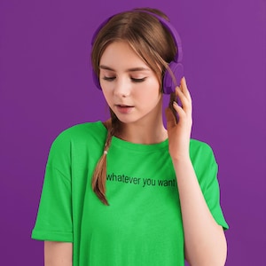 May include: A young person wearing a green t-shirt with the text "whatever you want" printed on it. They are wearing purple headphones and looking down.