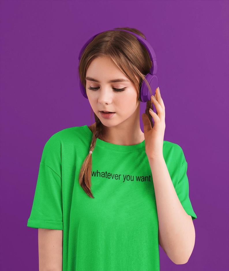 May include: A young person wearing a green t-shirt with the text "whatever you want" printed on it. They are wearing purple headphones and looking down.