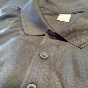 May include: Close-up of a dark gray polo shirt with a collar and two buttons. The shirt has the text "LIFE SIDE ELECTRICAL" in red letters on the upper left side.