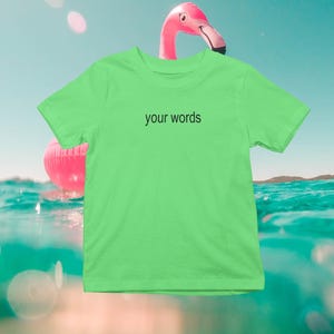May include: A bright green t-shirt with the text "your words" printed in black on the front. The t-shirt is photographed against a background of blue water and a pink flamingo float.