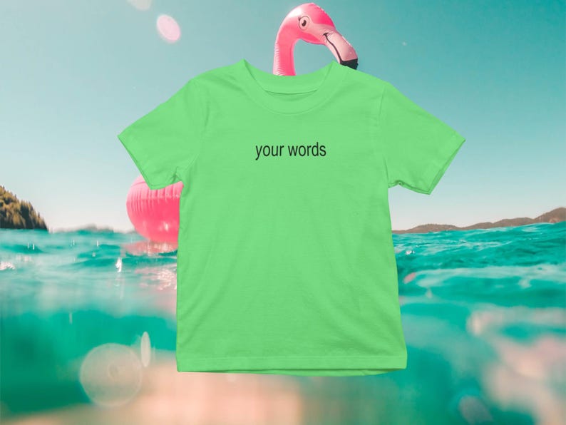 May include: A bright green t-shirt with the text "your words" printed in black on the front. The t-shirt is photographed against a background of blue water and a pink flamingo float.