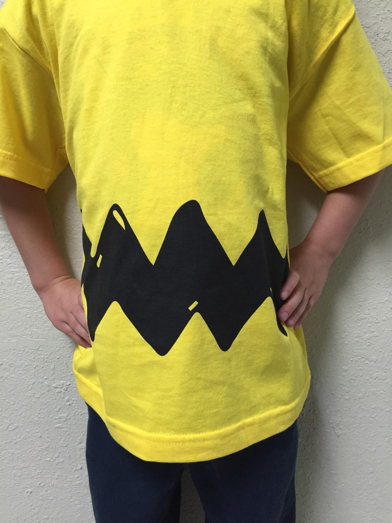 Peut inclure: Un t-shirt jaune avec un motif en zigzag noir en bas. Le motif ressemble au personnage embl&eacute;matique, Snoopy.