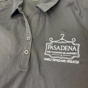 May include: Dark gray polo shirt with a collared neckline and three buttons. The shirt features the embroidered text "PASADENA DRY CLEANING & LAUNDRY" and "FAMILY OWNED AND OPERATED" in white.
