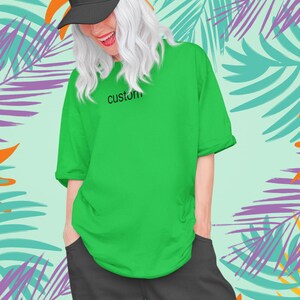 May include: A person wearing a green t-shirt with the word "custom" printed on the front. They are also wearing a black baseball cap and black pants. The background is a tropical print with palm leaves in shades of green, orange, and purple.