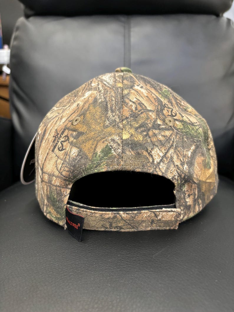 May include: A camouflage baseball cap with a black brim and a red "Realtree" logo on the back.