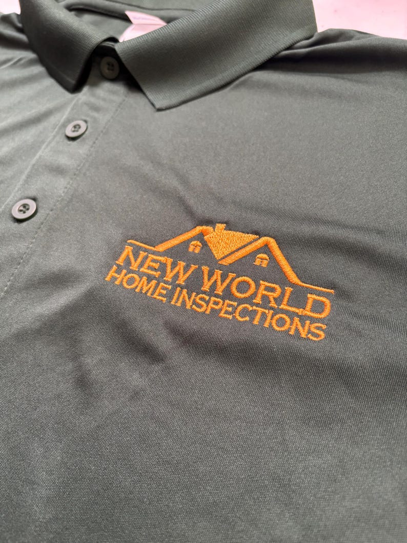 May include: Dark green polo shirt with a collar and three buttons. The shirt features the embroidered text "NEW WORLD HOME INSPECTIONS" in orange, along with a house logo. The shirt is made of a smooth, likely synthetic fabric.