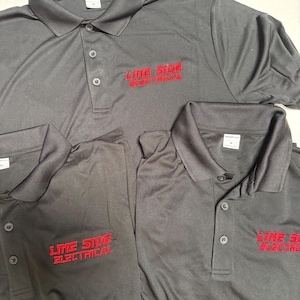 May include: Several dark gray polo shirts with the embroidered text "LINE SIDE ELECTRICAL" in red. The shirts have a collared neckline and buttoned placket. The shirts are made of a smooth, likely synthetic fabric.