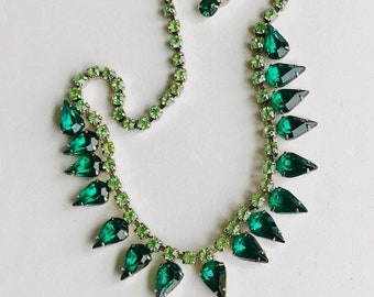May include: A vintage emerald green rhinestone necklace with a teardrop design. The necklace is made of silver tone metal and features a graduated row of teardrop-shaped rhinestones.