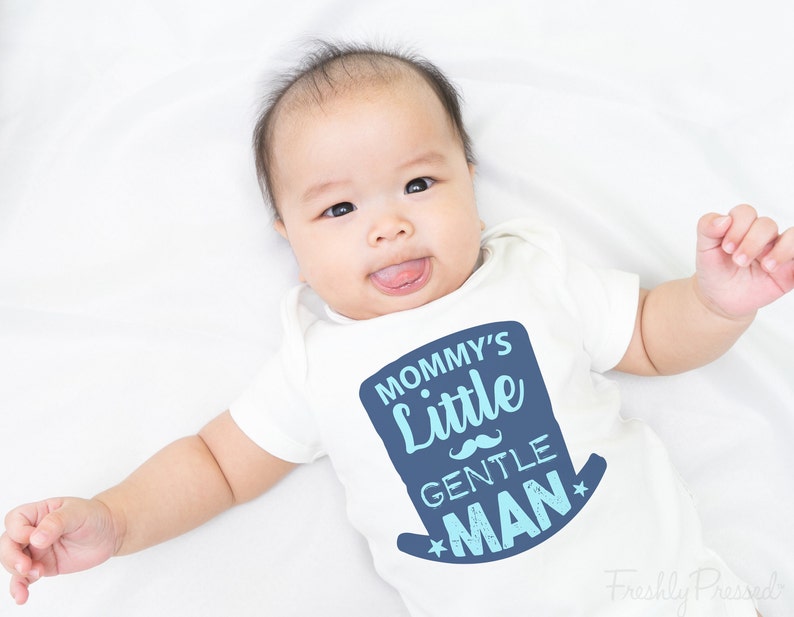 May include: A white baby onesie with a blue and light blue graphic that says "Mommy's Little Gentle Man" with a blue mustache and stars.