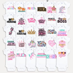 May include: A collection of thirty white baby bodysuits featuring various pink, gold, and multi-colored graphic designs with text including Pink Princess Baby Shower, I Am Loved, Born To Rule, Queen Of Cuddles, The Boss, and Sleeping Beauty.