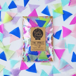 May include: A package of colorful tissue paper triangles labeled "Table Sprinkles" with the text "Freshly Pressed." The triangles are in shades of blue, pink, green, and purple. Each triangle is approximately 1 inch in size.
