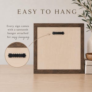 May include: A square wooden sign with a dark brown frame and a light beige centre panel. A black metal sawtooth hanger is attached to the back. Text on the image reads: EASY TO HANG. Every sign comes with a sawtooth hanger attached for easy hanging.