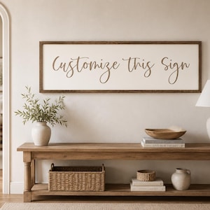 May include: A rectangular wall sign with a dark brown wooden frame and a cream-coloured background featuring the brown cursive text Customize This Sign centred on the surface. The sign is mounted horizontally on a plain wall above a wooden bench.