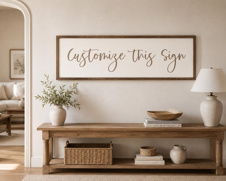 May include: A rectangular wall sign with a dark brown wooden frame and a cream-coloured background featuring the brown cursive text Customize This Sign centred on the surface. The sign is mounted horizontally on a plain wall above a wooden bench.