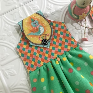 May include: A green tea towel with yellow polka dots and a hanging loop. The loop features a colorful fabric panel with a cartoon bird wearing a party hat.
