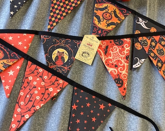 May include: A Halloween banner with black and orange fabric triangles. Each triangle features a different spooky design, including stars, pumpkins, owls, and bats. The banner is strung with black ribbon and has a tag that reads "Handmade in Ohio".
