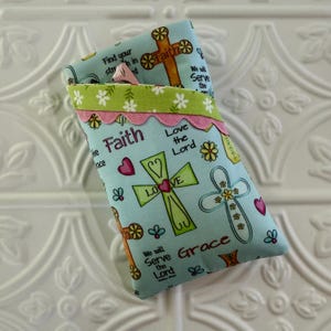 May include: Two light blue fabric pouches with religious text and cross designs. The pouches feature the words "Faith", "Love", and "Grace", along with decorative crosses, hearts, and flowers. The top edge has a green and pink trim.