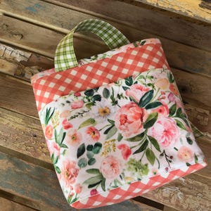 May include: A small, red and white gingham fabric tote bag with a floral print lining. The bag has a green and white gingham fabric handle.