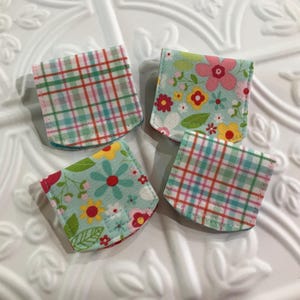 May include: Four small fabric pouches with different patterns. The pouches are made of a soft, cotton fabric and have a light blue background. The patterns include a plaid design, a floral design, and a floral design with a light blue background.