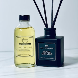 May include: A black glass bottle with a black label that reads "SOUL BATH COLLECTIVE ROOM DIFFUSER SOULBATHCOLLECTIVE.COM". A clear glass bottle with a black label that reads "SOUL BATH COLLECTIVE SOUL REVIVAL GRAPEFRUIT LEMON CITRON ROOM DIFFUSER OIL SOULBATHCOLLECTIVE.COM 4 OZ" is next to the black bottle. Black diffuser sticks are in the black bottle.