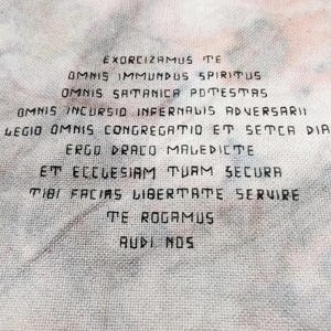 May include: A white fabric with black text that reads "EXORCIZAMUS TE OMNIS IMMUNDUS SPIRITUS OMNIS SATANICA POTESTAS OMNIS INCURSIO INFERNALIS ADVERSARII OMNIS LEGIO OMNIS CONGREGATIO ET SETCA DIABDUCA ERGO DRACO MALEDICTE ET ECCLESIAM TUAM SECURA TIBI FACIAS LIBERTATE SERVIRE TE ROGAMUS AUDI NOS".